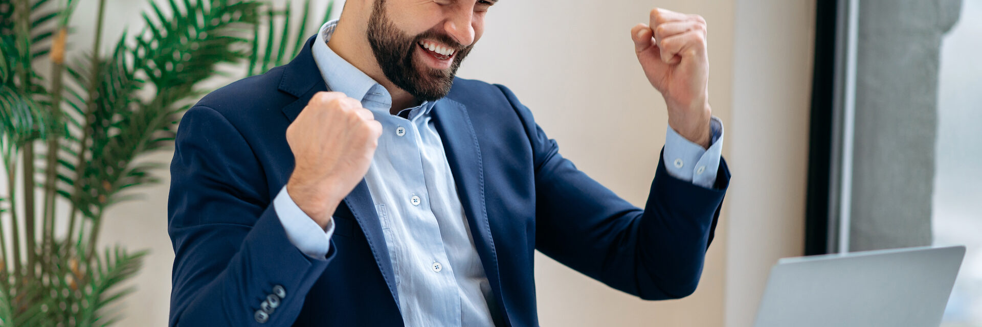 Successful joyful lucky caucasian businessman in a suit, ceo company, manager, sits at work desk in the office, gesturing with fists, celebrate success, win, big profit, good deal. Victory concept