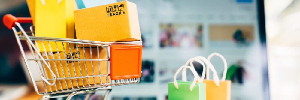 Product,Package,Boxes,And,Shopping,Bag,In,Cart,With,Laptop Kleine winkelwagen met stop tassen erin en ernaast op een laptop