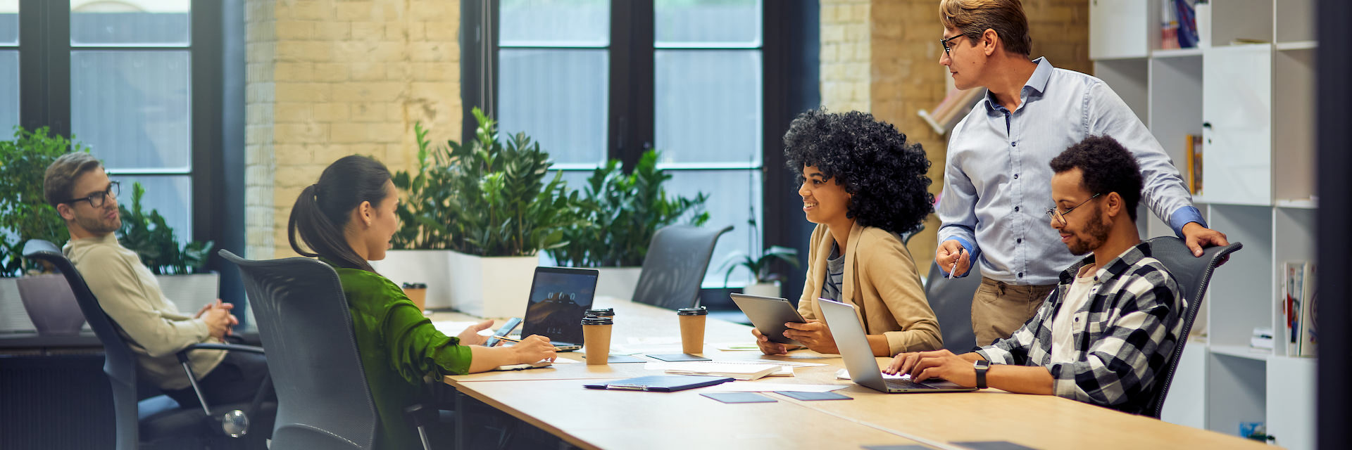 Office life. Group of young multiracial people sitting at the table in coworking space and working together, using modern technologies and discussing project mensen op kantoor